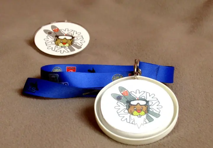 Jak zrobić medal dla dziecka? Dwa okrągłe medale z bobrem narciarzem i niebieska wstążka.