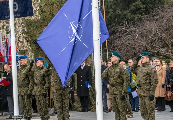 Uroczystość z flagą Organizacji Traktatu Północnoatlantyckiego. Żołnierze w mundurach oddają honory.