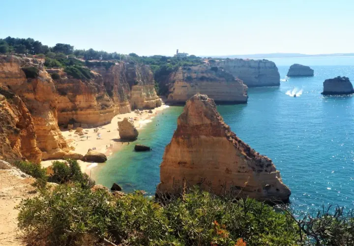 Acantilados dorados y aguas turquesas en una **playa** del **Algarve**. Gente disfrutando del sol y el mar.