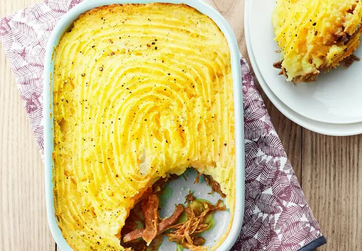 Un parmentier de canard doré et gratiné, prêt à être dégusté. Une portion est servie sur une assiette blanche.