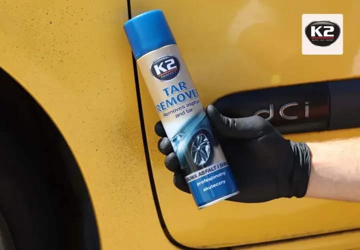 Rękawiczka z czarnym lateksem trzyma puszkę K2 Tar Remover, która pomoże Ci dowiedzieć się, czym usunąć asfalt z samochodu domowym sposobem.