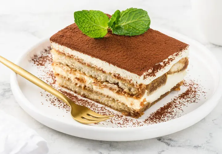 Pyszne, najprostsze tiramisu z kremem i biszkoptami, posypane kakao i udekorowane miętą. Złoty widelec czeka.