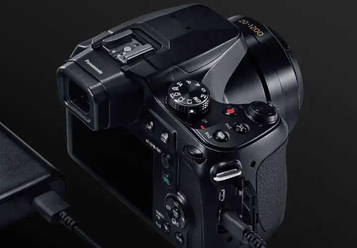 Czarny aparat Panasonic Lumix FZ82 z obiektywem 20-1200, podłączony do ładowarki.