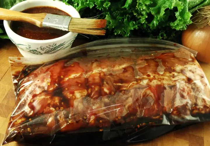Mięso w torbie z marynatą, gotowe do przygotowania pysznego beef jerky. Obok miseczka z marynatą i pędzelek.