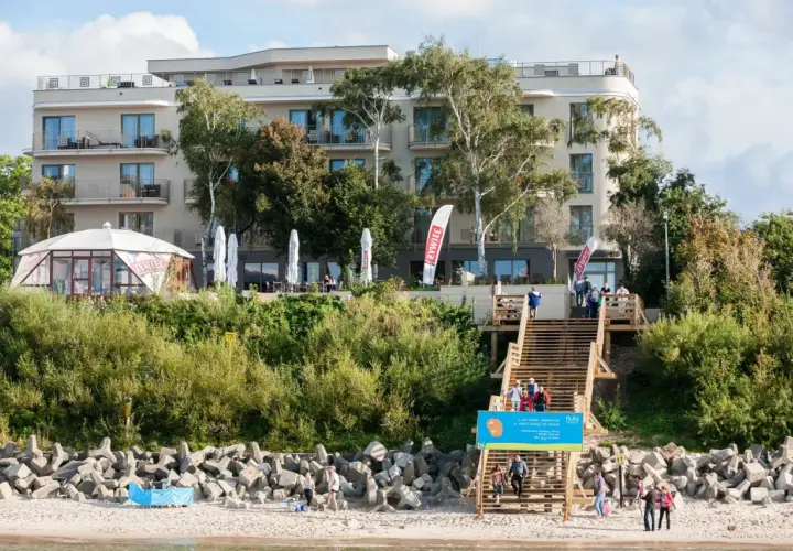 Hotel Lambert z tarasem i schodami prowadzącymi na plażę. Na schodach widać ludzi.