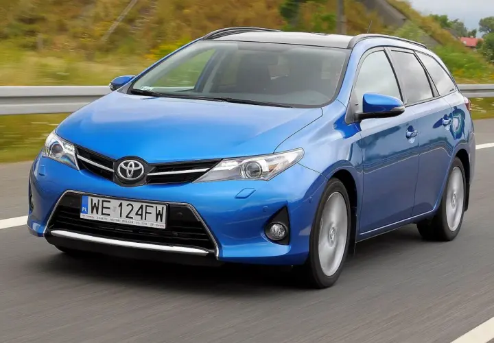 Niebieski Toyota Auris 1.6 benzyna w wersji kombi jedzie po drodze.