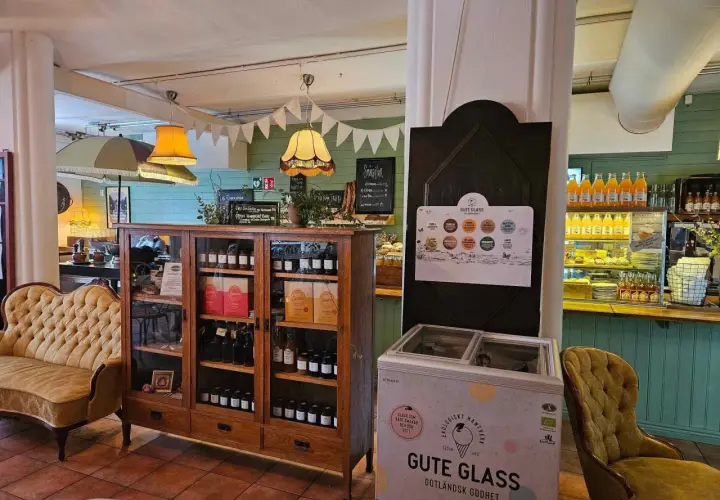 Mysigt café med en gul sammetssoffa, ett vitrinskåp fyllt med godsaker och en frys med "Gute Glass" Gotländsk godhet.
