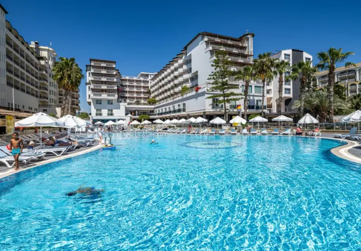 Basen hotelowy Granada Luxury Okurcalar, z leżakami, parasolami i palmami. Dzieci pluskają się w wodzie.