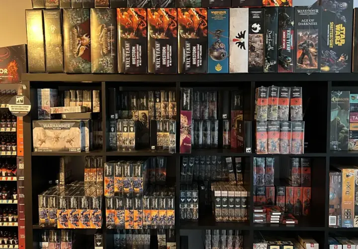 Półki pełne pudełek z grami i figurkami, w tym wiele z serii Warhammer. Widać tu zapowiedź przygód Gotreka i Felixa, a także inne tytuły.
