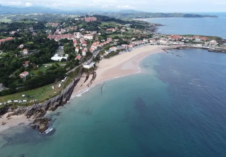 Vista aérea de la **playa de Comillas**, con sus casas, acantilados y el mar Cantábrico.