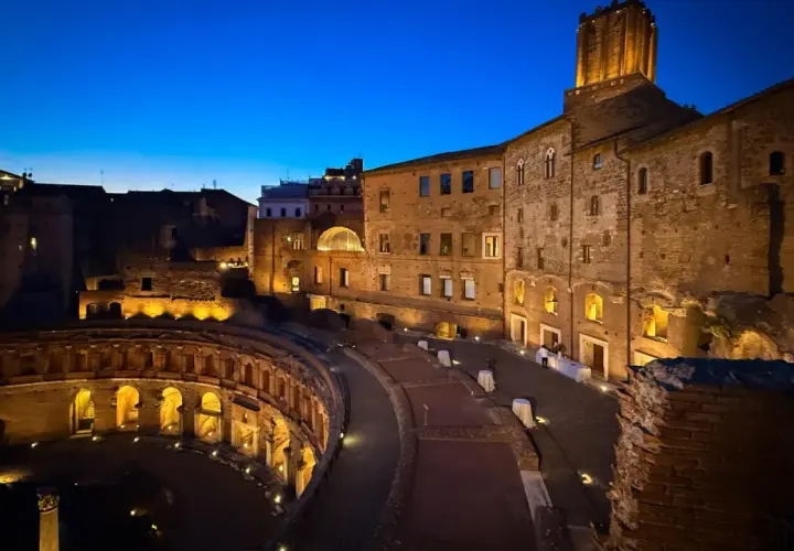 Il mercato di Traiano illuminato di notte, con le sue antiche mura di mattoni e l'arco semicircolare, evoca un'atmosfera magica.