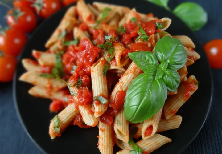 Penne rigate z sosem pomidorowym i świeżą bazylią, ozdobione listkami bazylii.
