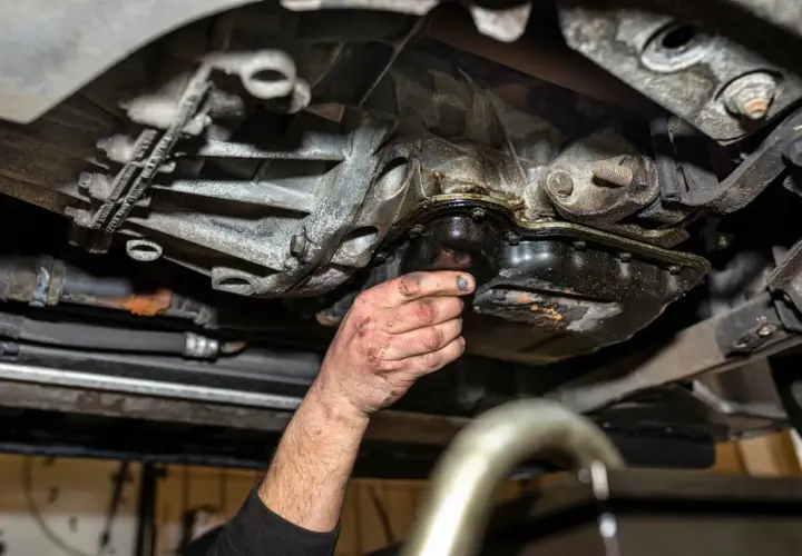 Ręka mechanika sprawdza szczelność miski olejowej. Widać wycieki oleju i zabrudzenia.