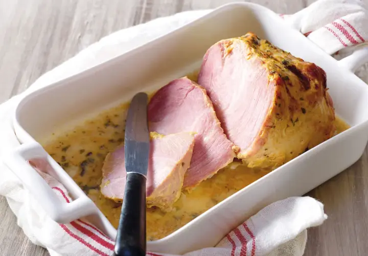 Palette à la diable, tranchée et servie dans un plat blanc avec une sauce dorée. Un couteau est posé sur la viande.