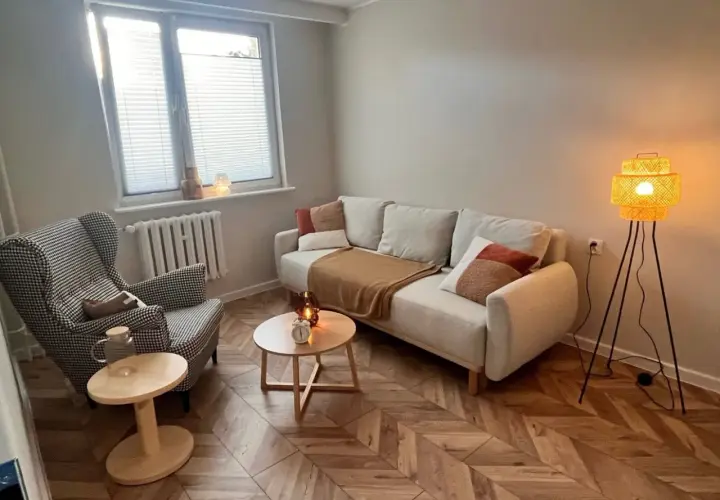 Przytulny gabinet terapeutyczny z sofą, fotelem i lampą.