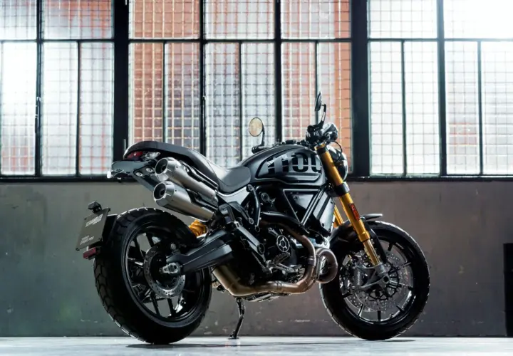 Czarny motocykl Ducati Scrambler 1100 Sport Pro, jeden z najlepszych motocykli, stoi przed industrialnymi oknami.