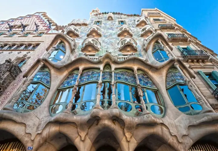 Façade d'un bâtiment à l'architecture organique, avec un **art nouveau motif végétal** sculpté dans la pierre et des vitraux bleus.