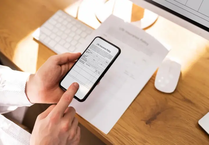 Dłoń trzyma smartfon, który działa jak darmowy skaner dokumentów, skanując polisę ubezpieczeniową.
