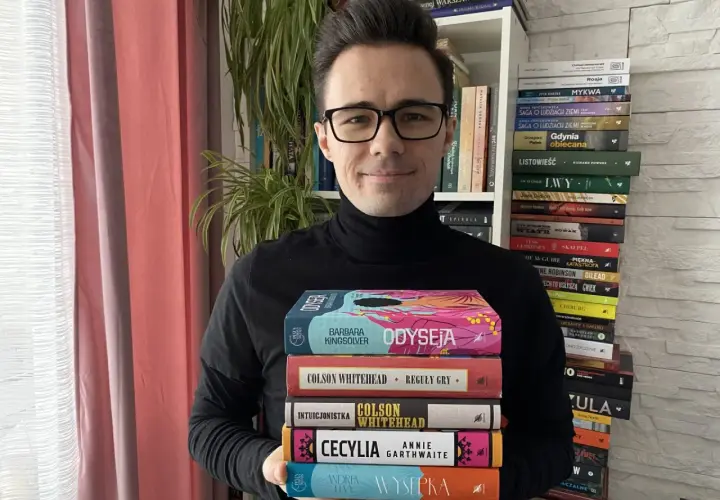 Mężczyzna w okularach trzyma stos książek, wśród nich "Odyseja" i "Reguły gry". To dowód na bogactwo polskiej myśli szkoleniowej.