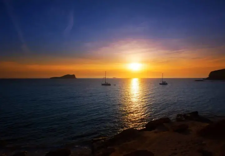 Un atardecer mágico en Ibiza, con veleros navegando y el sol tiñendo el mar de oro. Un lugar perfecto donde ver el atardecer en Ibiza.