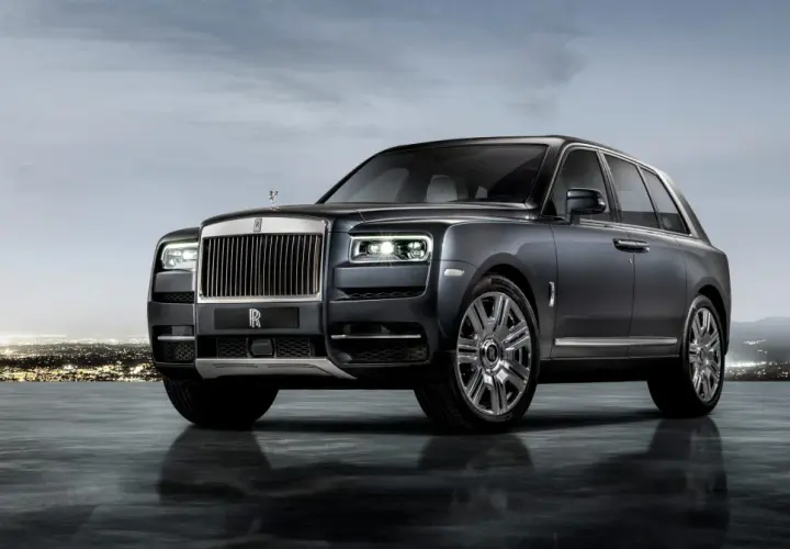 Elegancki Rolls-Royce SUV w ciemnym kolorze, lśniącym na tle nocnego miasta i gór.