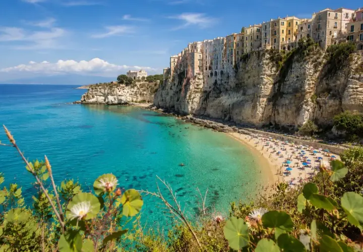 A vibrant beach scene on the Calabria coast, with colorful buildings perched on dramatic cliffs overlooking turquoise waters.