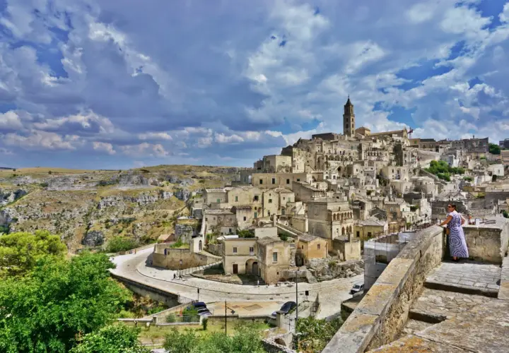 A woman in a patterned dress surveys the ancient Sassi di Matera, Italy. This view offers a glimpse of what to do in Matera Italy: explore its unique cave dwellings and historic architecture.
