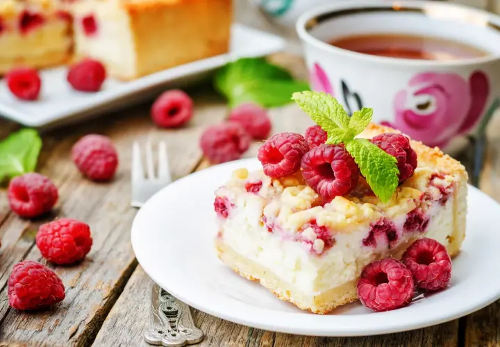 Malinowa chmurka z serem i malinami, udekorowana listkiem mięty, na talerzyku obok filiżanki herbaty.