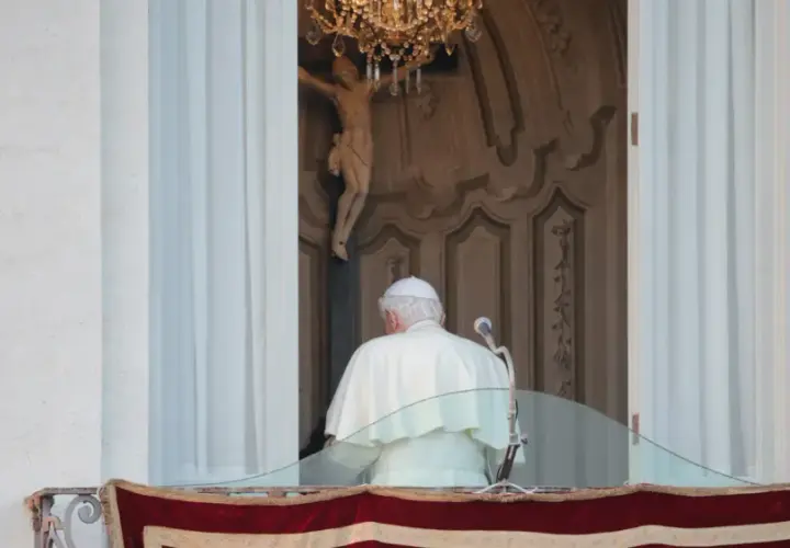 Der Papst steht auf dem Balkon, hinter ihm ein Kruzifix und ein Kronleuchter.