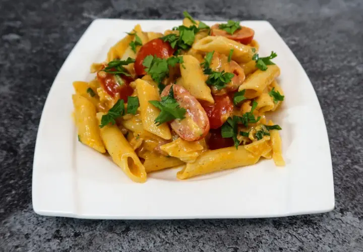 Penne z kremowym sosem serowym, kawałkami chrupiącego boczku i pomidorkami koktajlowymi, posypane świeżą natką pietruszki.