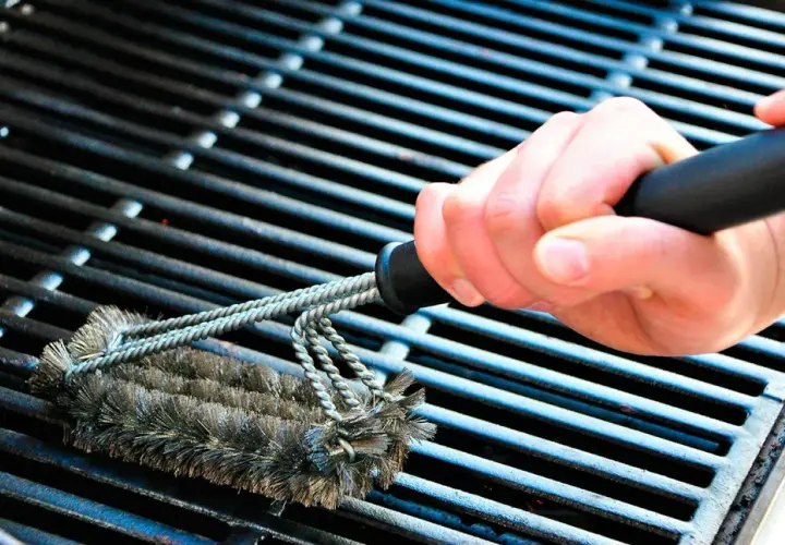 En hand använder en grillborste för att rengöra grillen. Avfettning behövs för att få bort envis smuts.