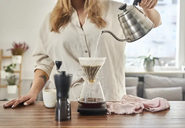 Kobieta przygotowuje kawę metodą v60 drip. Gorąca woda powoli przelewa się przez zmielone ziarna do dzbanka.