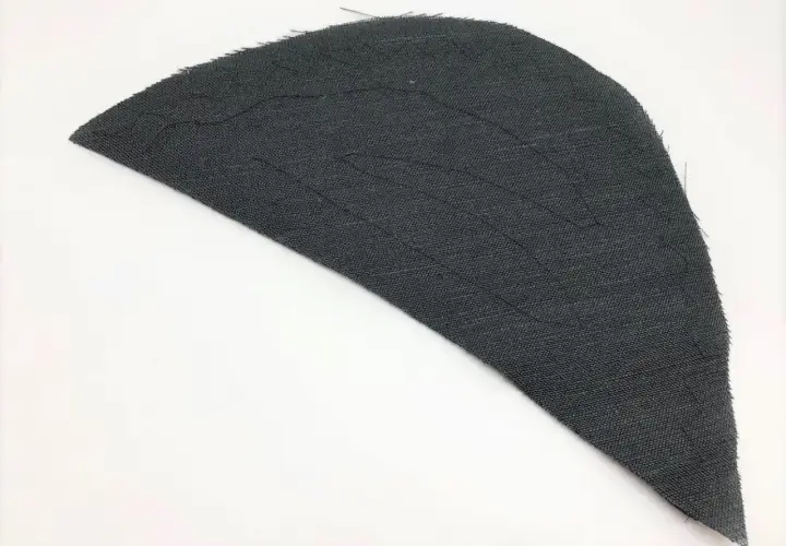 A dark gray fabric piece, shaped like a wing, shows stitching lines that form a shoulder pad pattern.