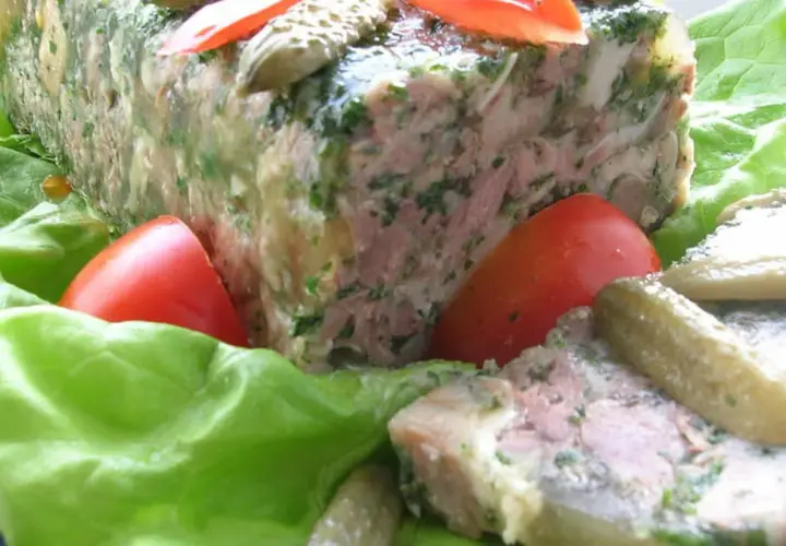 Tranche de pâté de tête maison, garnie de persil, servie sur des feuilles de laitue avec des tomates et des cornichons. Un délice pour une recette de pâté de tête.