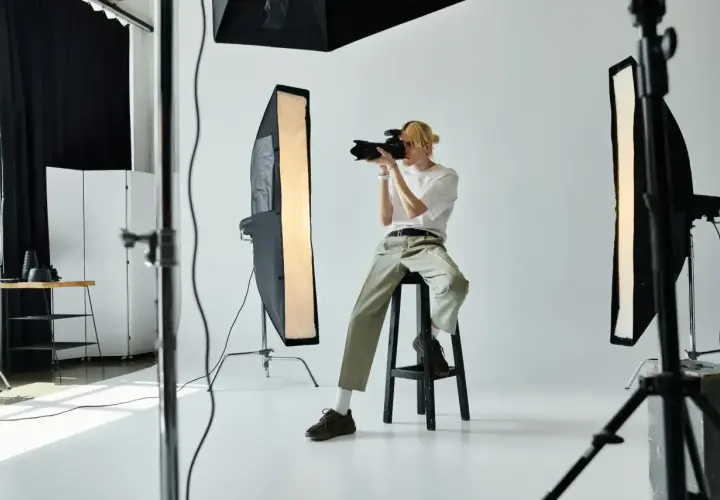 Młody fotograf w studio, z aparatem w ręku, zastanawia się, ile zarabia fotograf.