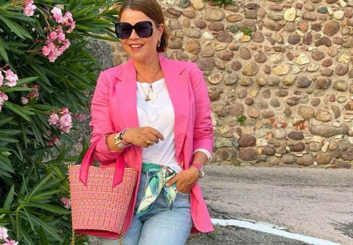 Kobieta w różowej marynarce i jeansach, z torebką i apaszką, tworzy idealny outfit na randkę.
