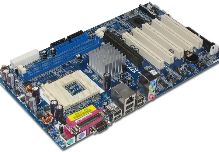 Carte mère d'ordinateur bleue avec dissipateur thermique, connecteurs RAM, PCI et ports d'entrée/sortie.