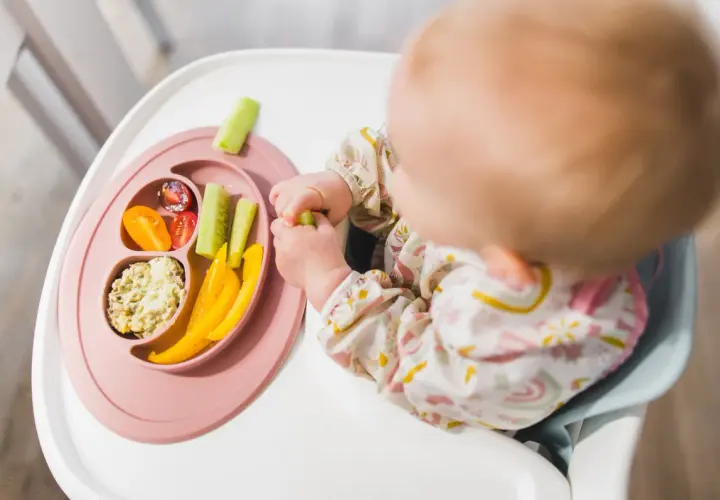 Dziecko odkrywa smaki warzyw, stosując metodę blw. Na talerzyku: pomidorki, ogórek, papryka i pasta.