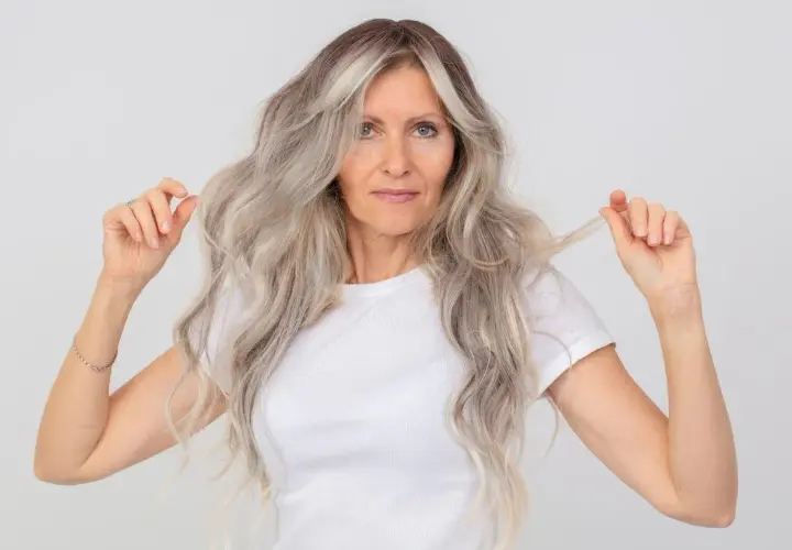 Mujer con cabello largo y ondulado, con mechas grises y rubias. Muestra cómo matizar el pelo en casa para un look radiante.