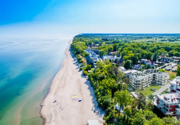 Idealny pobyt nad morzem: piaszczysta plaża, turkusowa woda i nowoczesne apartamenty wśród zieleni.