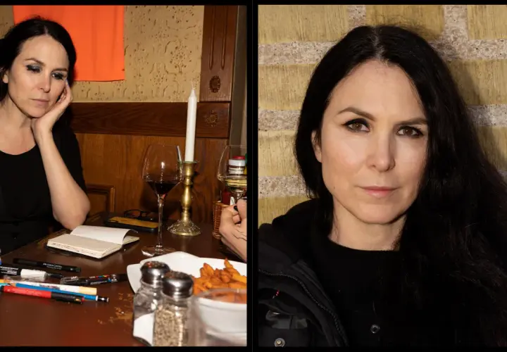 Nina Hemmingsson, med sitt karakteristiska uttryck, sitter vid ett bord med pennor och ett glas rödvin.