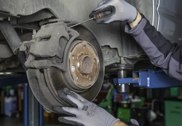 Mechanik w rękawiczkach sprawdza hamulce, by uniknąć bicia kierownicy przy hamowaniu.