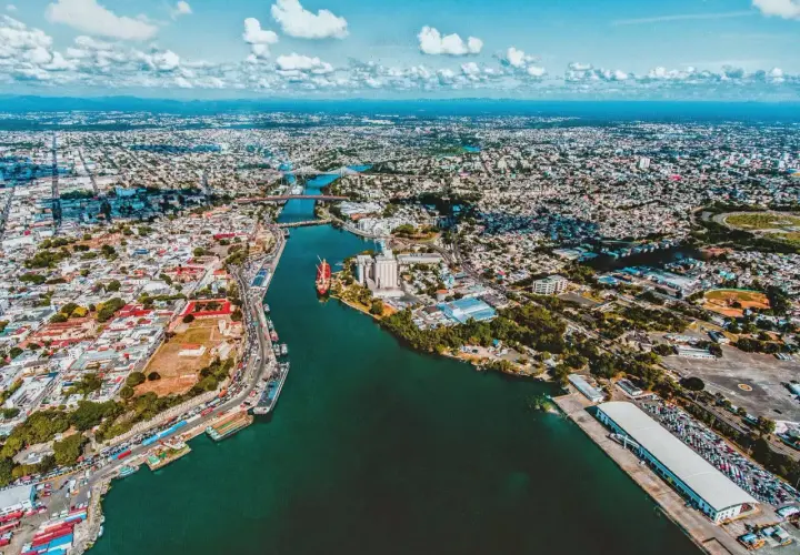 Luftaufnahme der Stadt mit einem Fluss, der sich durch sie schlängelt. Hier ist, wo Santo Domingo liegt, mit Schiffen im Hafen und vielen Gebäuden.