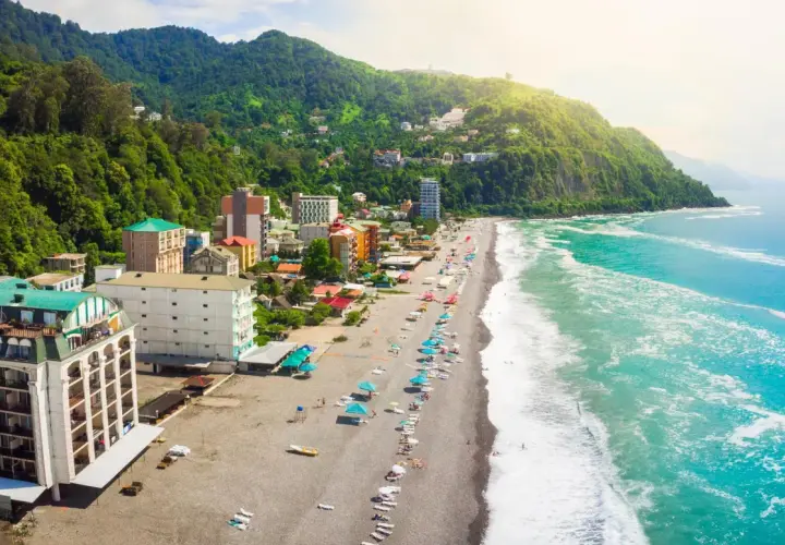 Widok na wybrzeże Gruzji, z zielonymi wzgórzami, kolorowymi budynkami i piaszczystą plażą nad turkusowym morzem.