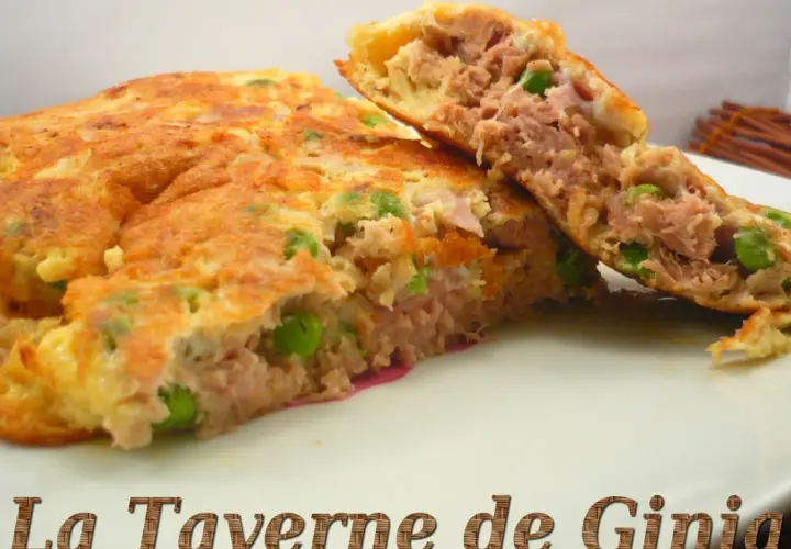 Une omelette au thon généreuse, garnie de petits pois, coupée en deux pour révéler sa texture moelleuse. Un délice simple et savoureux.