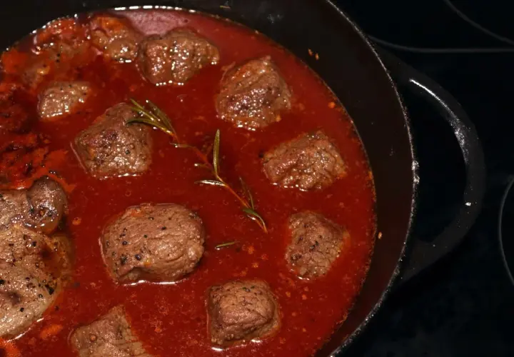 Stracotto di manzo schmort in einer tiefroten Sauce mit Rosmarin. Zarte Fleischstücke, perfekt für ein herzhaftes Gericht.