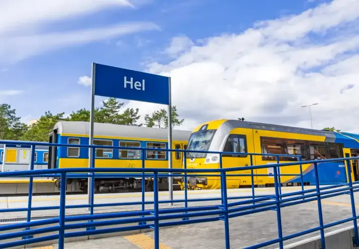 Pociąg z Władysławowa do Helu stoi na stacji. Żółto-niebieskie wagony czekają na pasażerów.