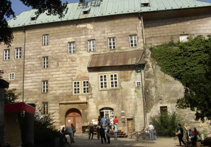 Kamienny zamek Houska z zielonym dachem i licznymi oknami, otoczony zielenią.