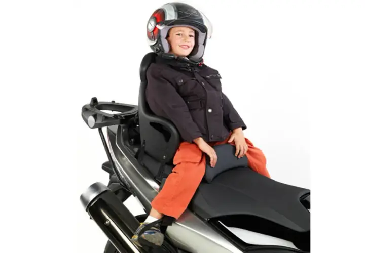Niño sonriente con casco en asiento de moto. ¿A qué edad puede ir un niño en moto? Depende de la normativa y el equipo.