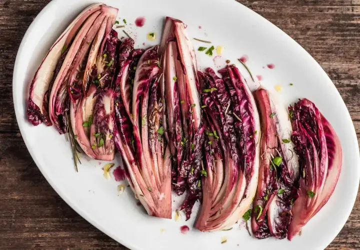 Radicchio al forno, tagliato a spicchi e condito con erbe aromatiche, servito su un piatto bianco.